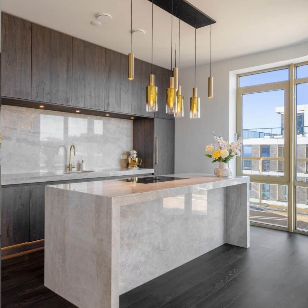 Impressie van een luxe keuken, voorzien van glanzend marmer met gouden aders, dat we terugzien als aanrechtblad, de achterwand van een nis en het kookeiland.