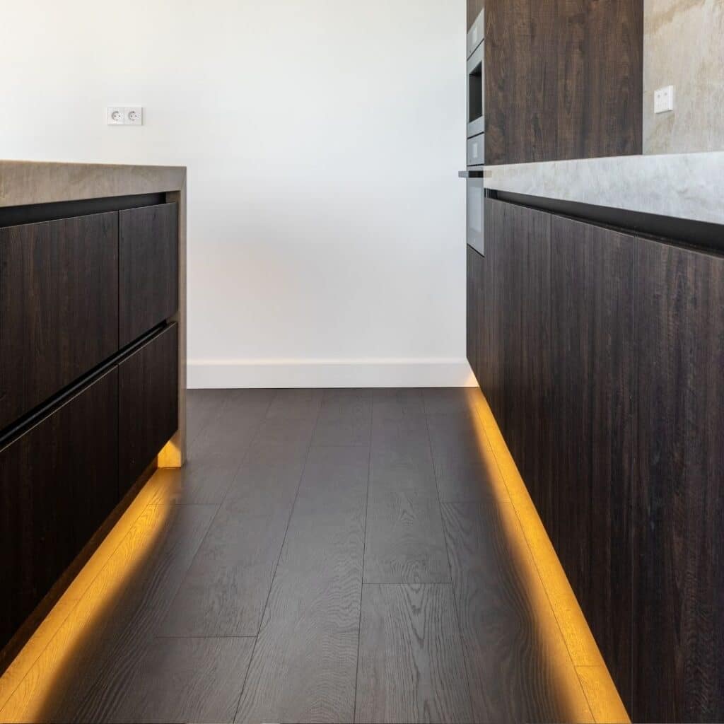 Impressie van een luxe keuken met houten vloer. Onder de kastenwand en het eiland die warm licht afgeven.