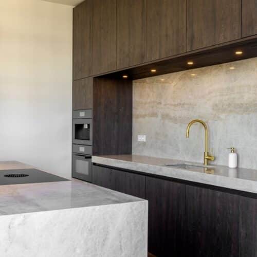 Impressie van een luxe keuken, voorzien van een kookeiland en keuken nis in glanzend marmer met gouden aders.