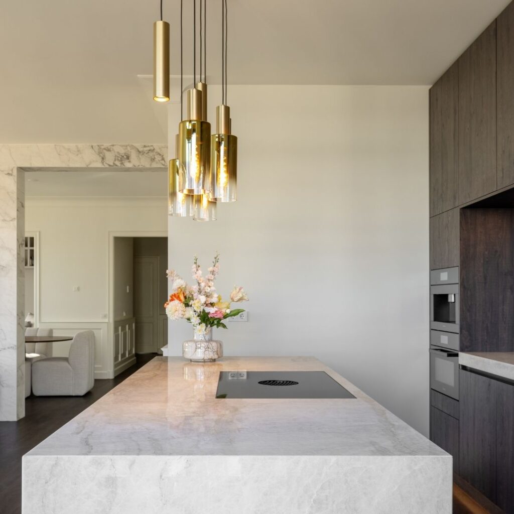 Impressie van een luxe keuken, voorzien van kookeiland in glanzend marmer met gouden aders. Op het kookeiland zien we een Bora kookplaat. Erboven hangen design plafondlampen in de kleur goud.
