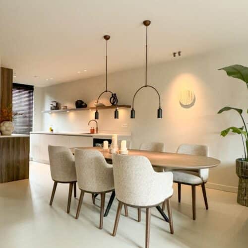 Impressie van een benedenverdieping met een Japandi keuken in een parallel opstelling. De keuken is ingericht met een strak werkblad, veel opberglades, een Quooker, een wijnklimaatkast en houten kastenwand.