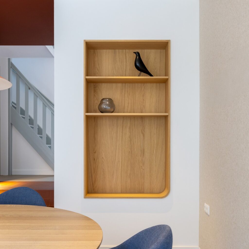 Impressie van een rechthoekige houten nis, voorzien van drie hoeken en een afgeronde hoek. De nis heeft twee planken met decoraties.