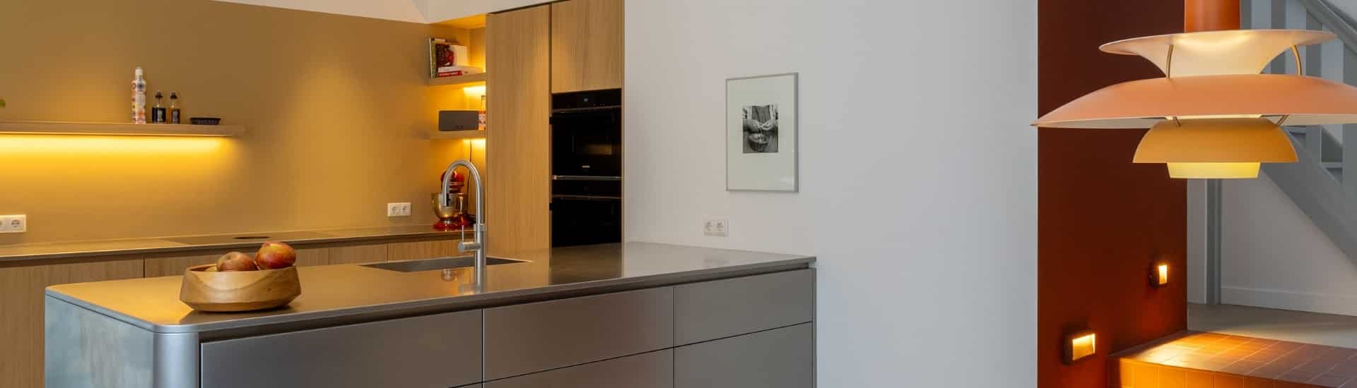 Impressie van een design keuken, voorzien van houten kasten, een RVS schiereiland en sfeervolle verlichting en decoraties.