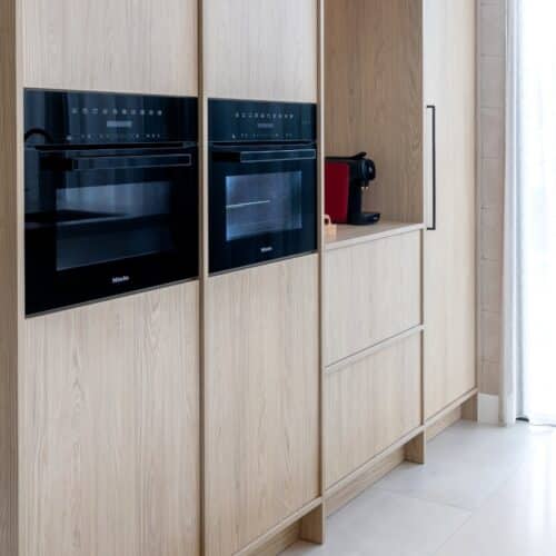 Impressie van een Japandi stijl keuken met licht eiken kastenwand, voorzien van Miele ovens.