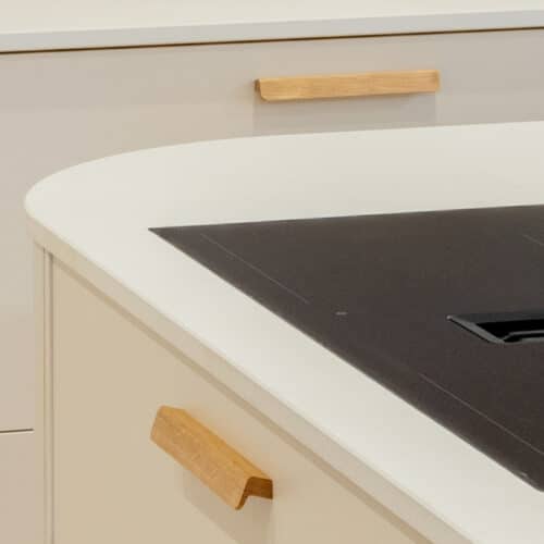 Impressie van een wit kookeiland met ronde hoeken, houten handgrepen en een Miele kookplaat met werkbladafzuiging.