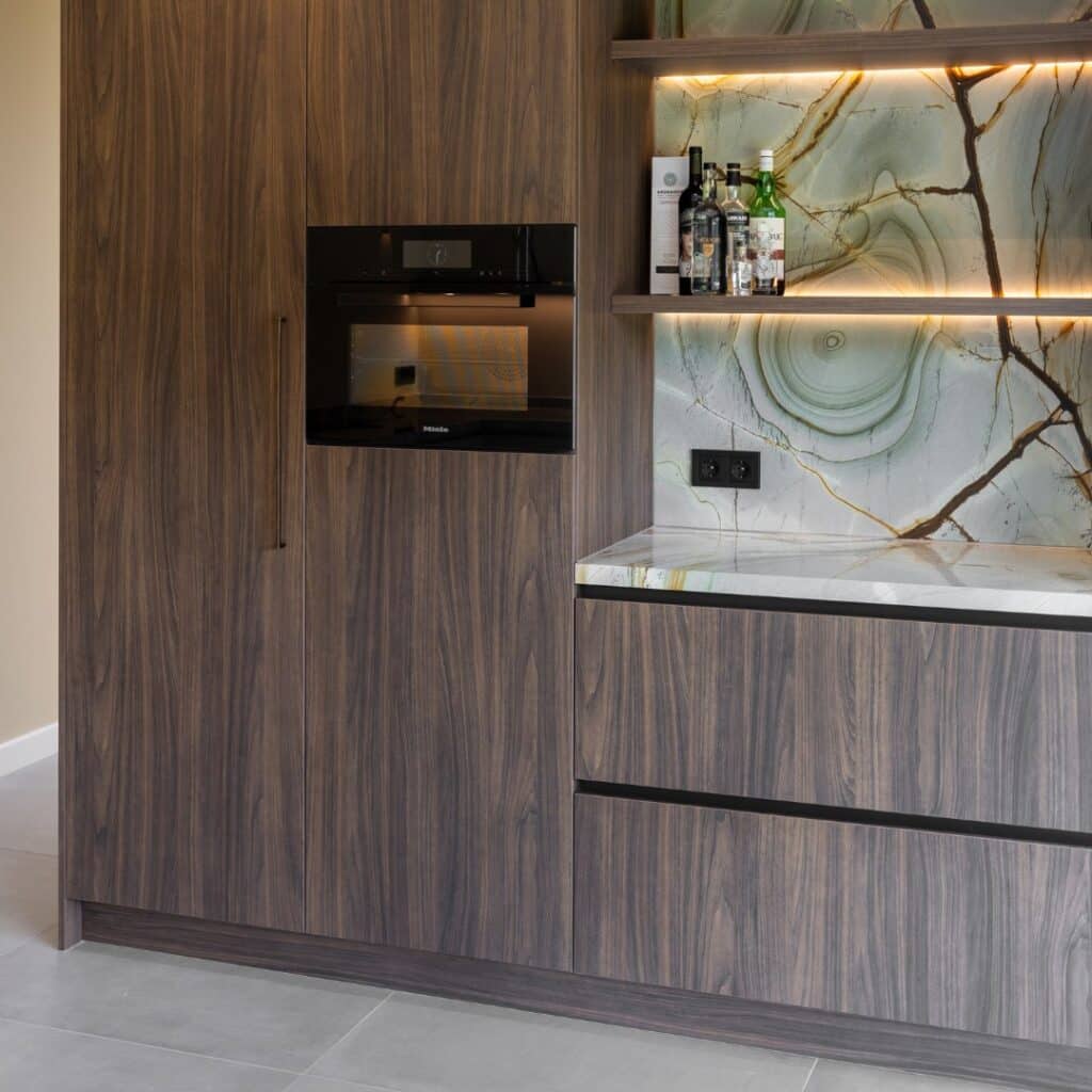 Close-up van een notenhouten kast, met een nis met marmer werkblad en kastdeur met handgreep in warme aardetint.