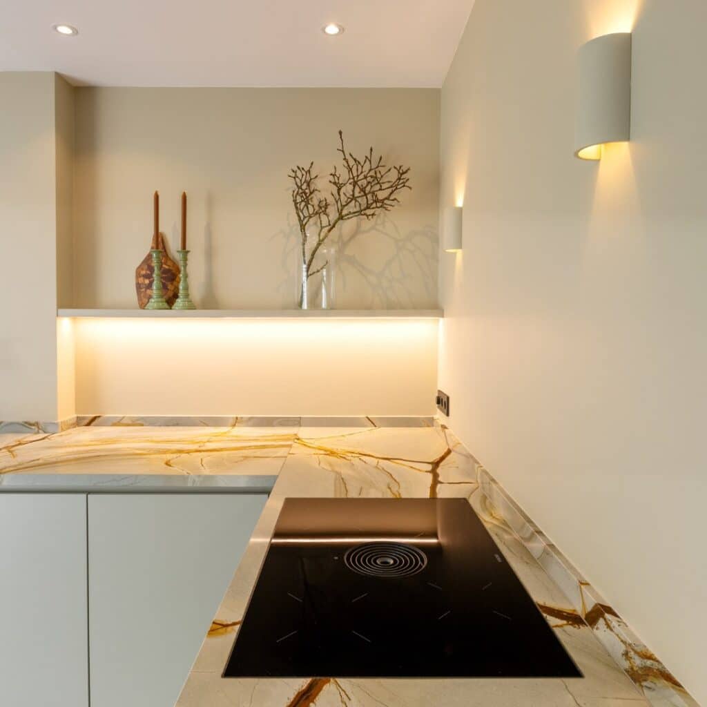 Impressie van een luxe keuken met rustige kleuren, voorzien van marmer werkblad en kookplaat met werkbladafzuiging.