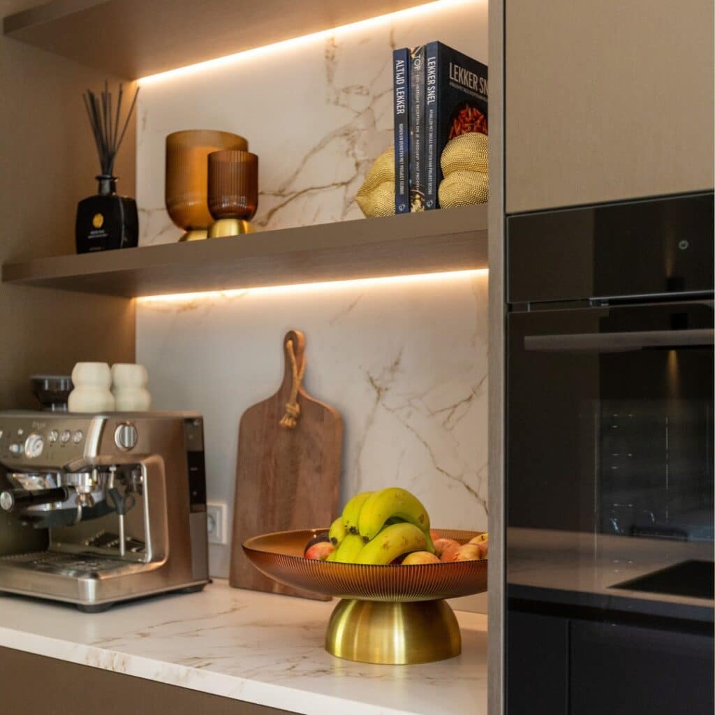 Impressie van een nis met blad en achterwand met patronen van marmer. De nis is ingericht met een koffiemachine, keukenspullen, een houten wandplank en twee ledstrips.