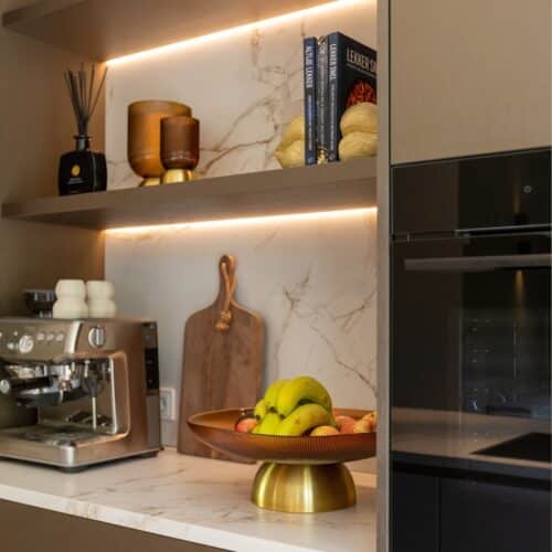 Impressie van een nis met blad en achterwand met patronen van marmer. De nis is ingericht met een koffiemachine, keukenspullen, een houten wandplank en twee ledstrips.