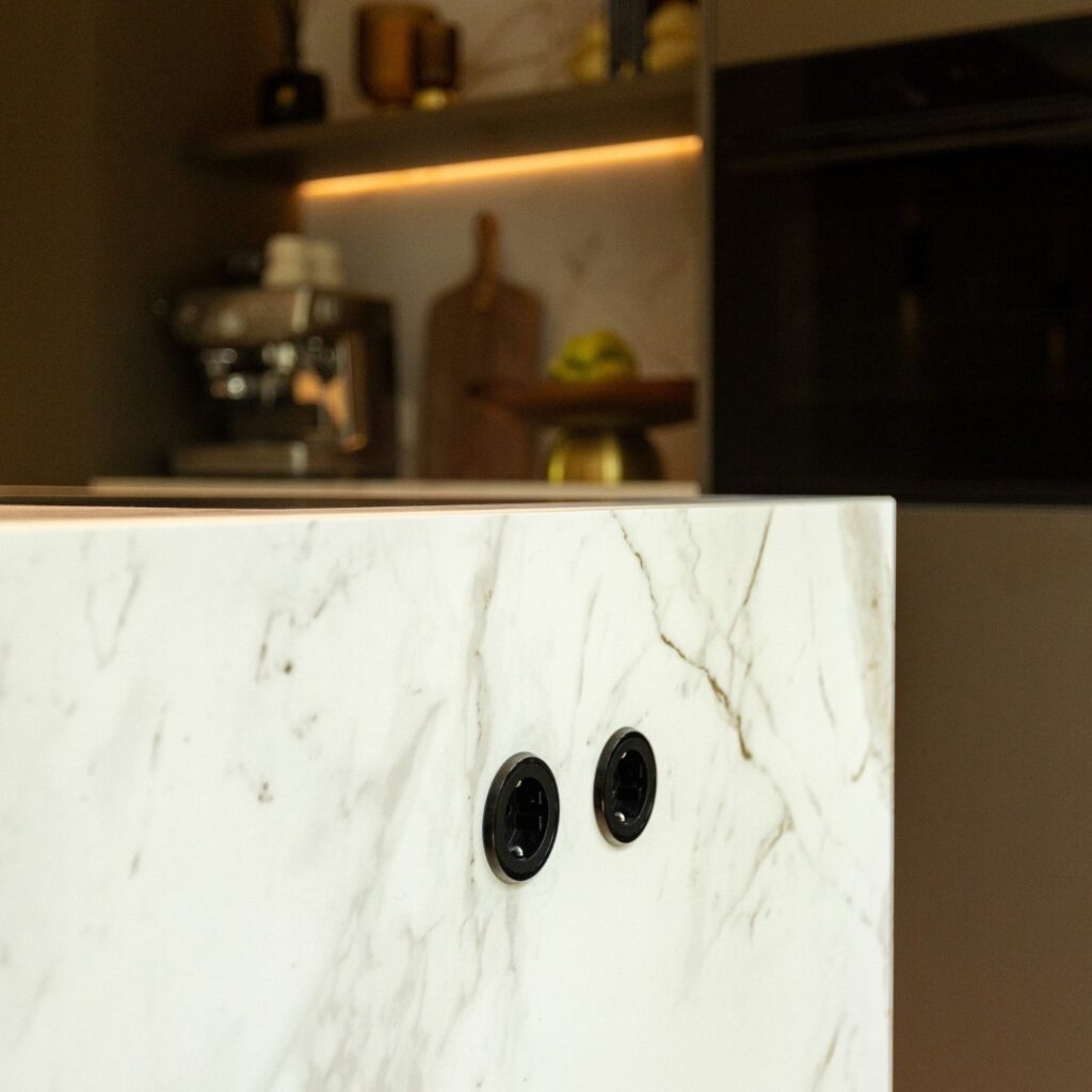 Close-up van een zijwand van een kookeiland. De wand is wit, met een zwart marmer patroon.