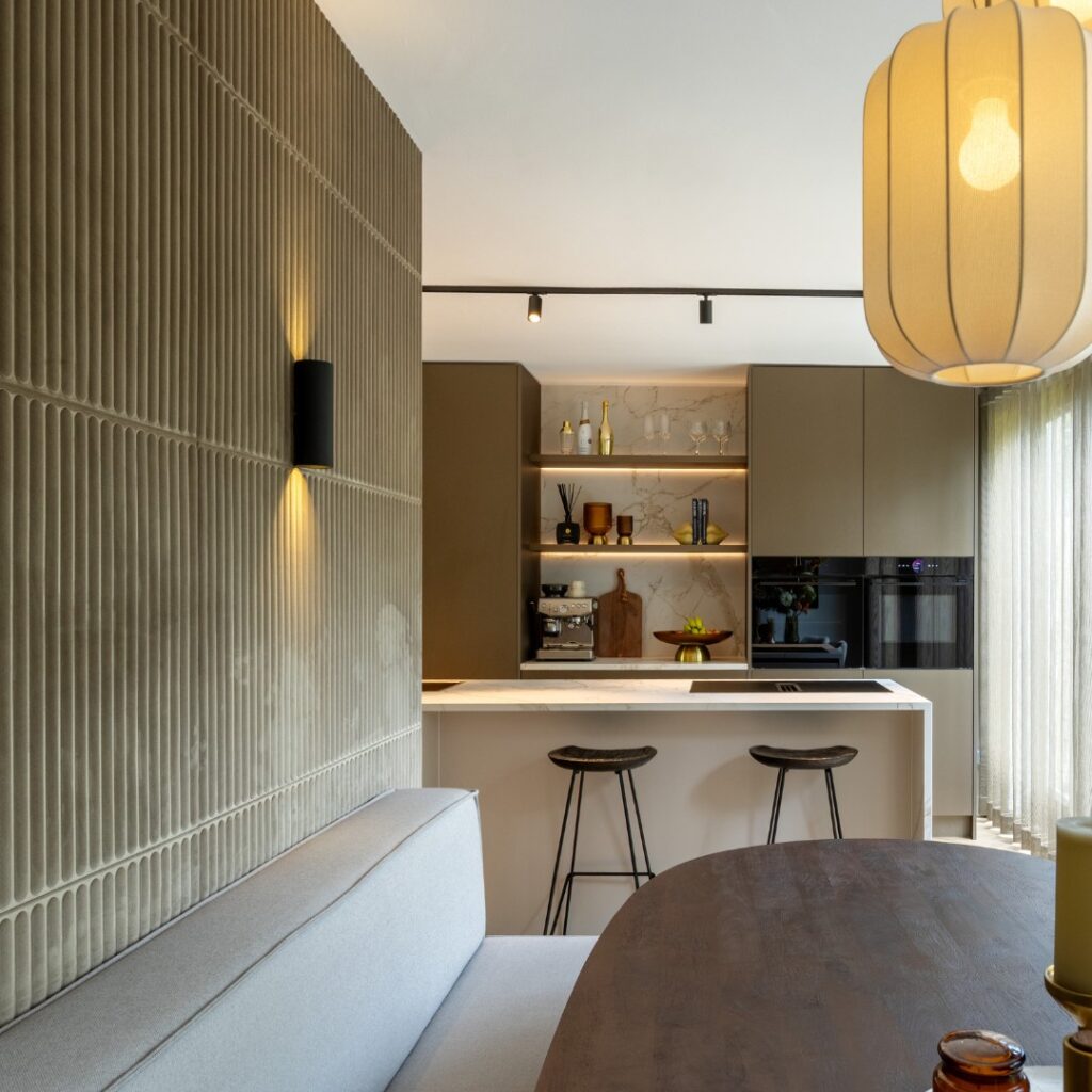 Kijk vanuit een eethoek naar een luxe keuken, voorzien van kookeiland met bar en een houten kastenwand met nis.