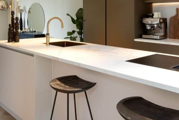 Impressie van een luxe keuken, voorzien van een kookeiland met bar. Het eiland heeft een marmerlook blad, met kookplaat en wasbak met Quooker in messing patina finish.