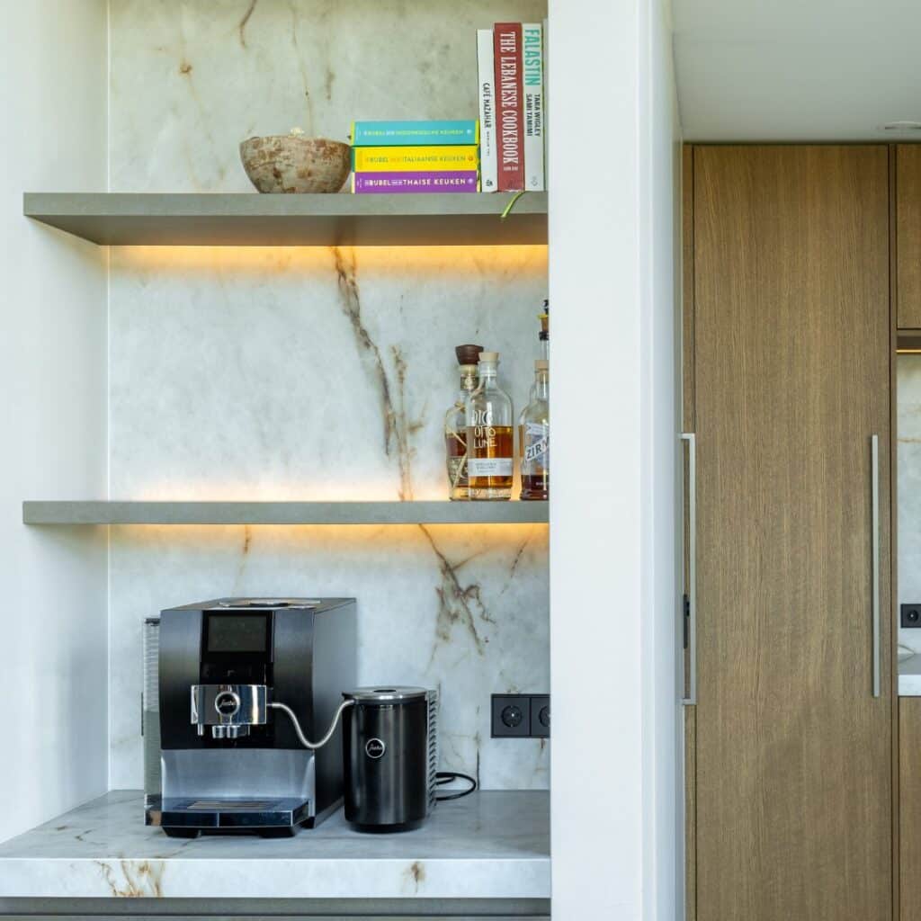 Impressie van een koffiecorner met een marmerlook blad en achterwand. De koffiehoek is ingericht met een koffiemachine en twee planken met ledstrips.
