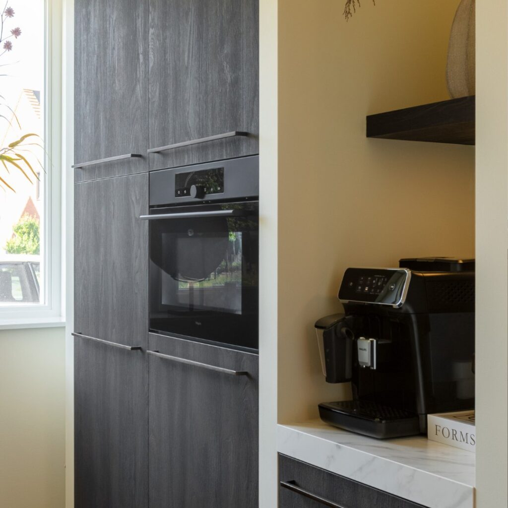 Impressie van een houten kastenwand in zwart, voorzien van een inbouwoven en nis met koffiemachine.
