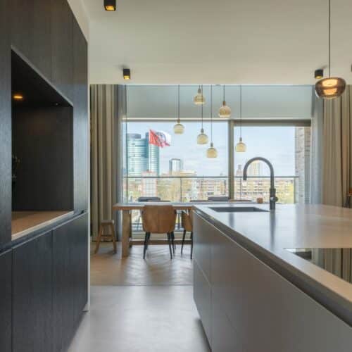 Impressie van een zwart-wit keuken met kookeiland en kastenwand met nis.