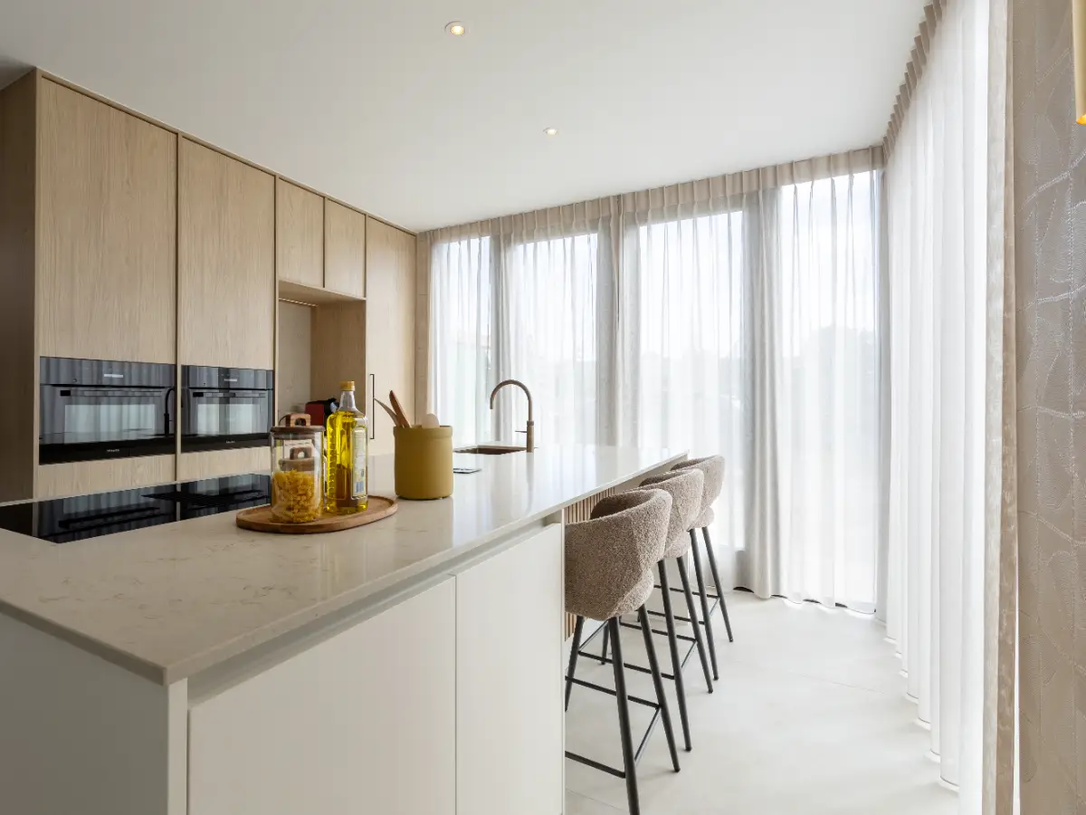 Scandinavisch design keuken met licht eikenhouten kasten, een wit kookeiland met barkrukken en grote ramen met transparante gordijnen.