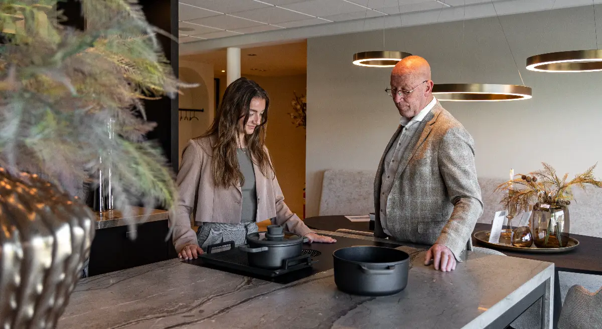 Keukenadviseur van Van Ginkel Keukens toont een luxe kookeiland met geïntegreerde inductiekookplaat en werkbladafzuiging in de showroom